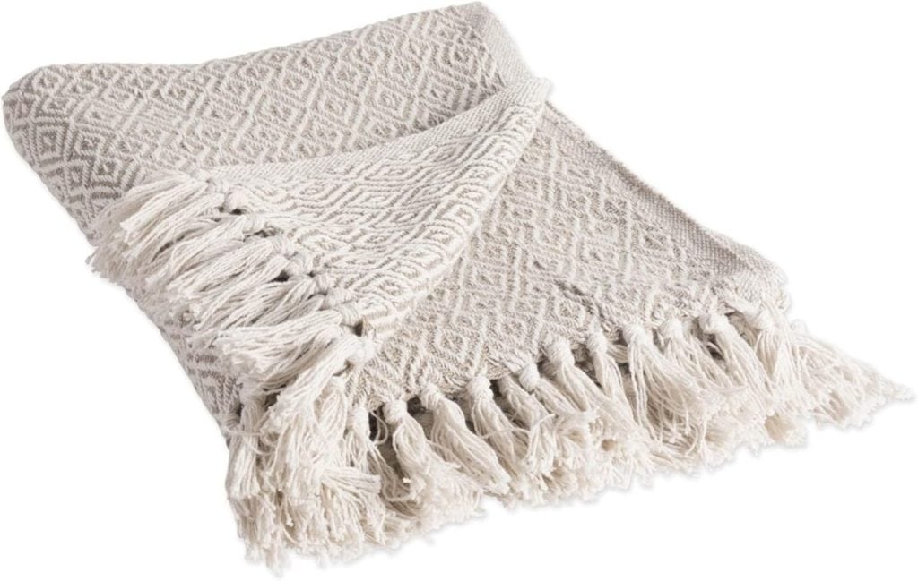 A folded beige throw blanket with a diamond pattern and fringed edges.