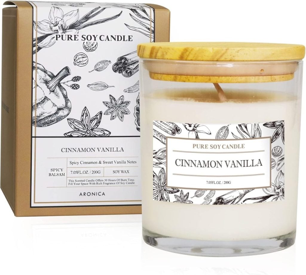 Candle labeled "Cinnamon Vanilla" in a glass jar with a wooden lid, next to its box featuring spice illustrations. Contains 7.05 fl. oz. of soy wax.