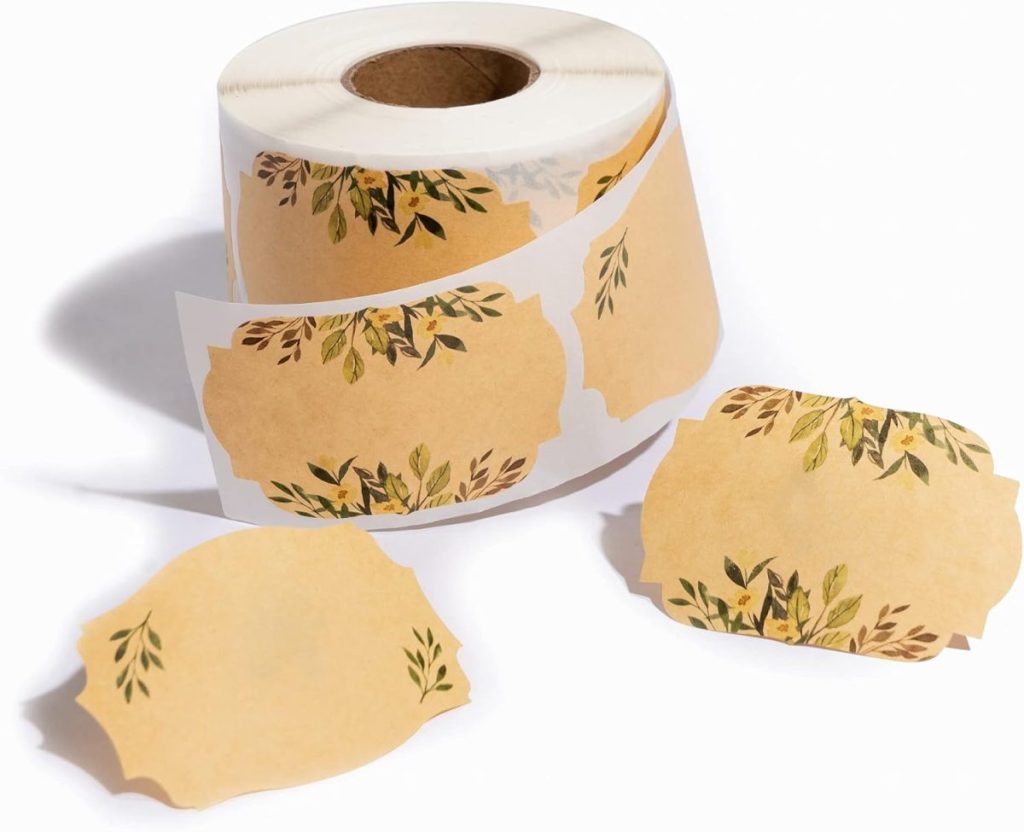 Roll of decorative label stickers with a floral design, featuring leaves in green and yellow on a beige background, perfect for embellishing your glass water bottles. Some labels are detached and artfully arranged in front of the roll.