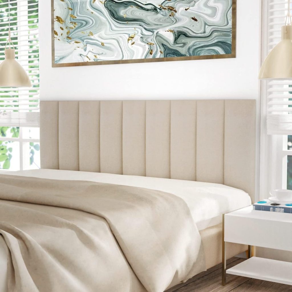 A neatly made bed with a beige headboard, a white nightstand with a blue book and glasses, and a green and gold abstract painting on the wall.