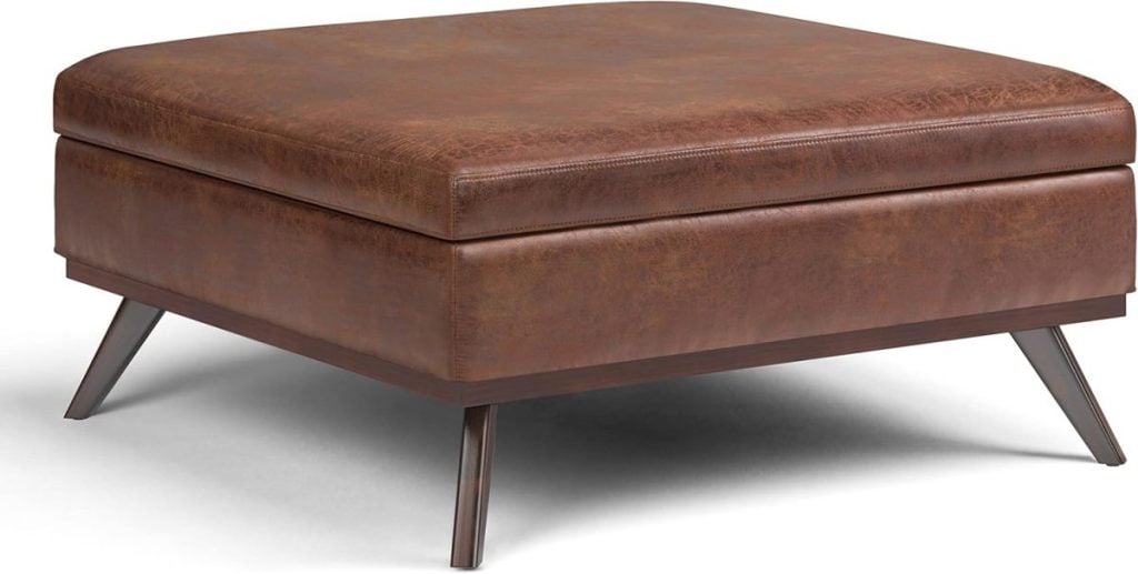 A brown leather ottoman with a square shape and tapered dark wooden legs.