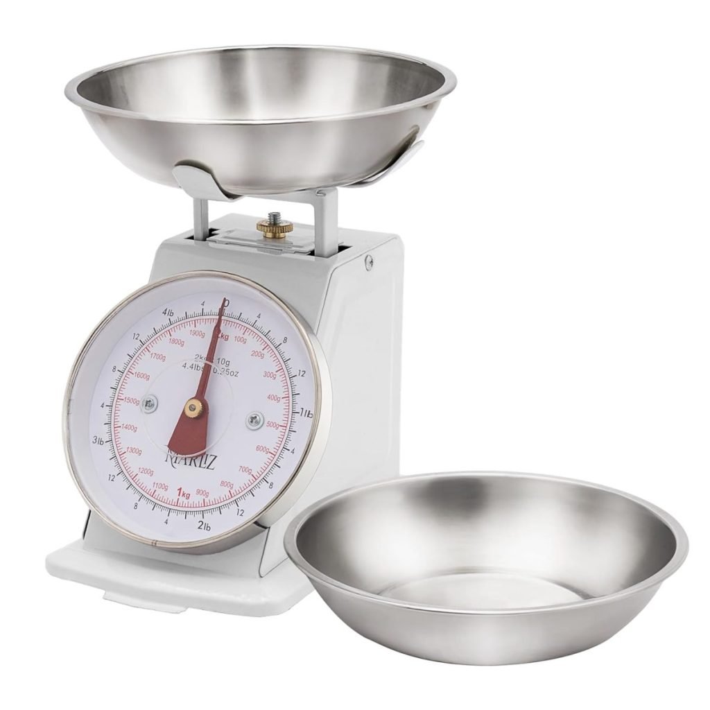 A stainless steel mechanical kitchen scale with a round dial and a removable bowl on the top, accompanied by another empty bowl placed next to it.