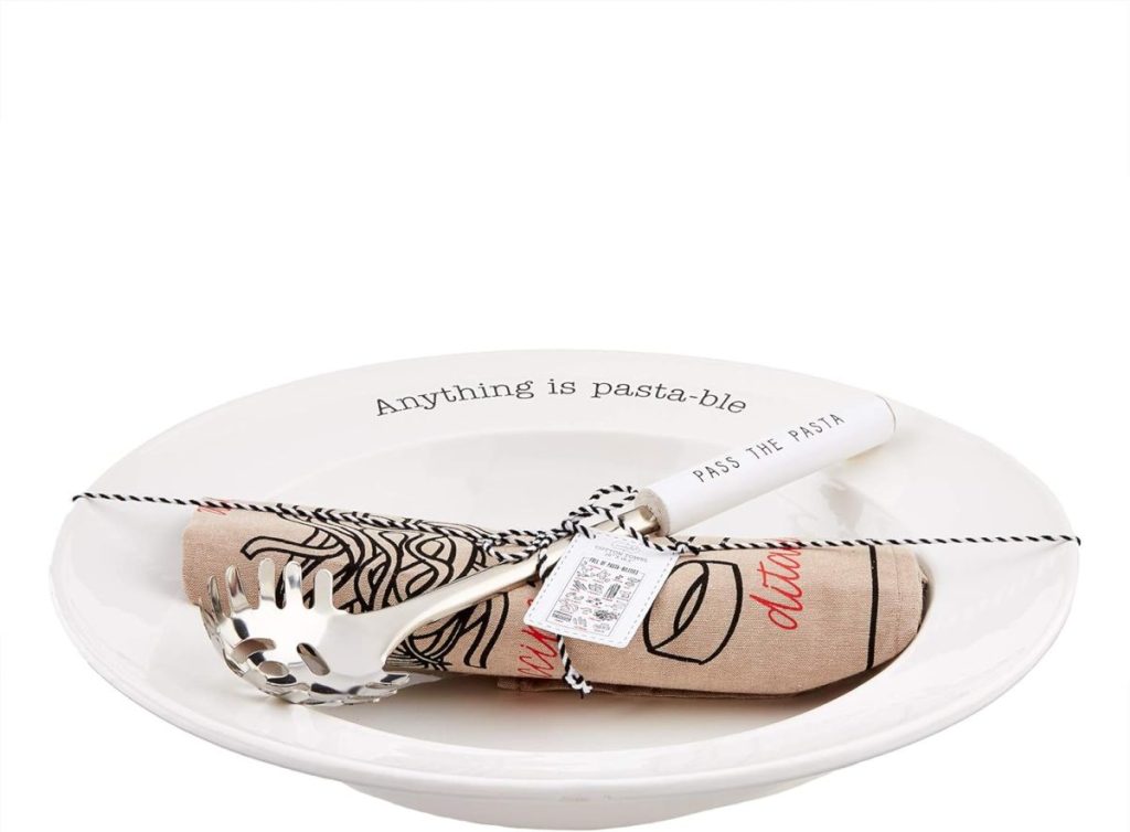 A white pasta bowl with the phrase "Anything is pasta-ble," holding a pasta serving utensil and a rolled beige napkin printed with fettuccini illustrations, tied together with black and white string.