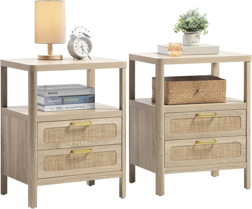 Two light-colored wooden nightstands with drawers. Each has items on top: one with a lamp and clock, the other with a plant and candle holder. Books and a wicker basket are on the open shelves.