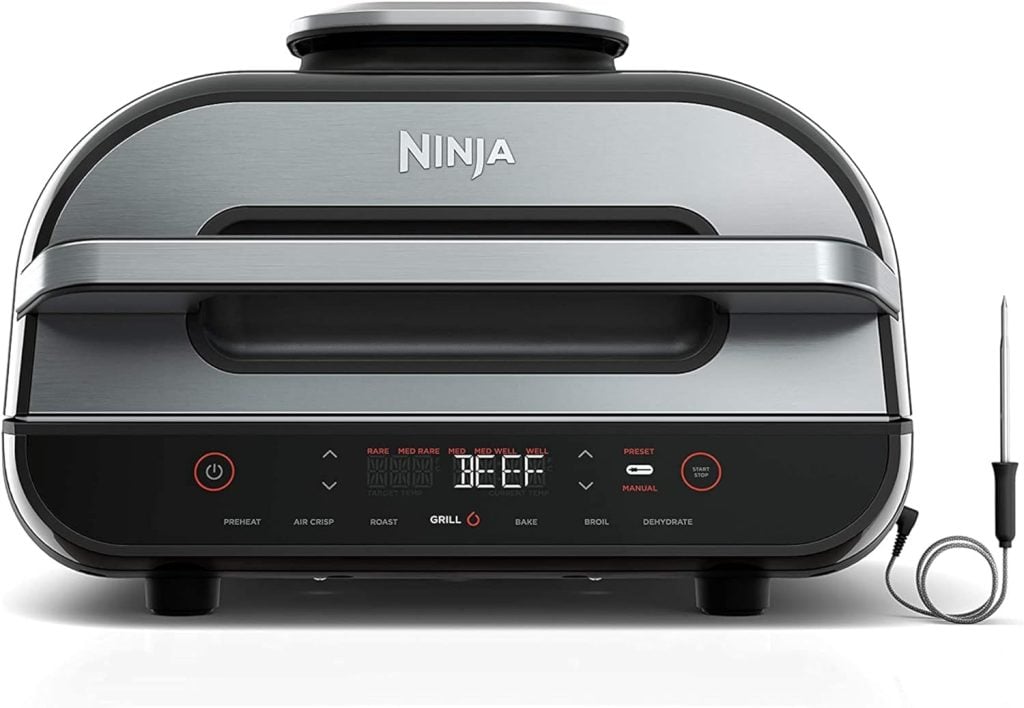 A sleek, silver Ninja Foodi grill with digital controls and a temperature probe attached, set on a white background.