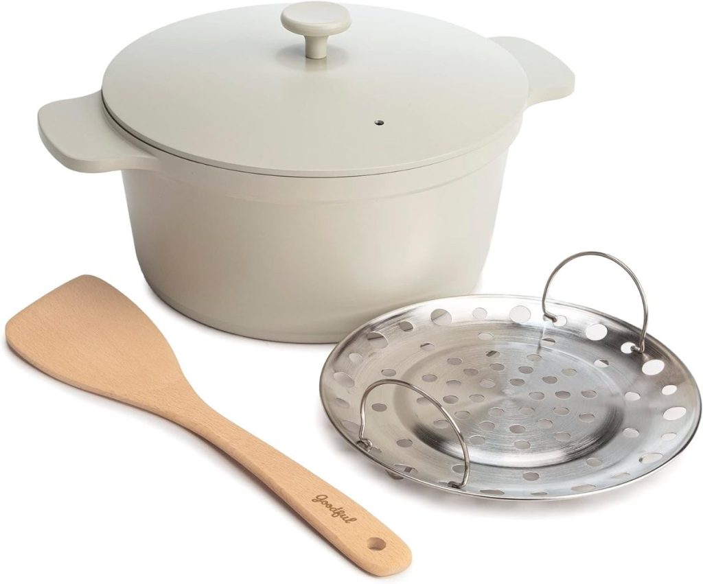 A beige cooking pot with a lid, accompanied by a wooden spatula and a round metal steamer insert, is artfully presented on a white background, ready for your next culinary adventure. Discover this and more kitchen essentials with the convenience of Amazon Prime.