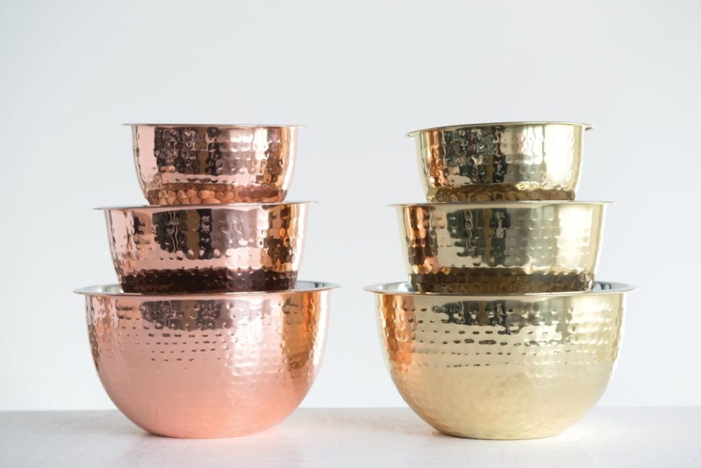 Six hammered metal mixing bowls, three copper-colored stacked on the left and three gold-colored on the right, are set on a white surface—perfect for prepping your next pear and cranberry tart against a plain background.