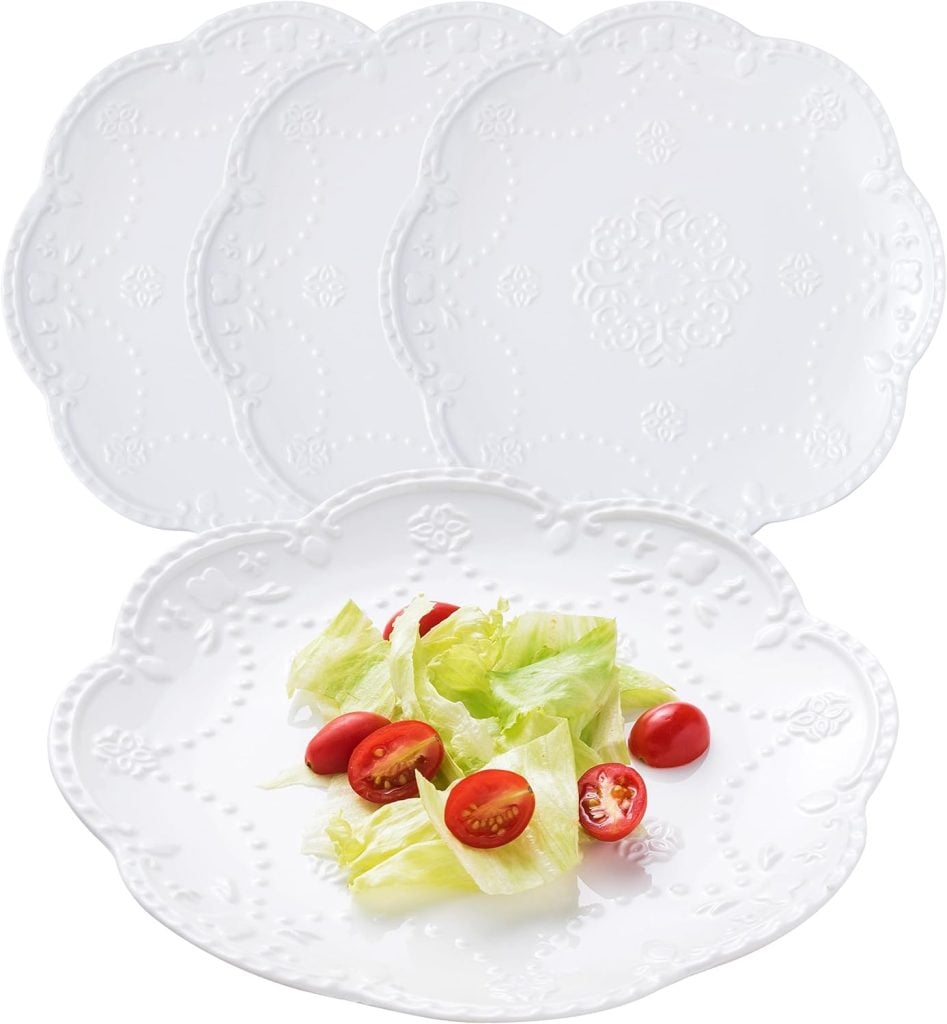 Four decorative white Thanksgiving plates with embossed patterns, one elegantly holding a salad of crisp lettuce and vibrant cherry tomatoes.