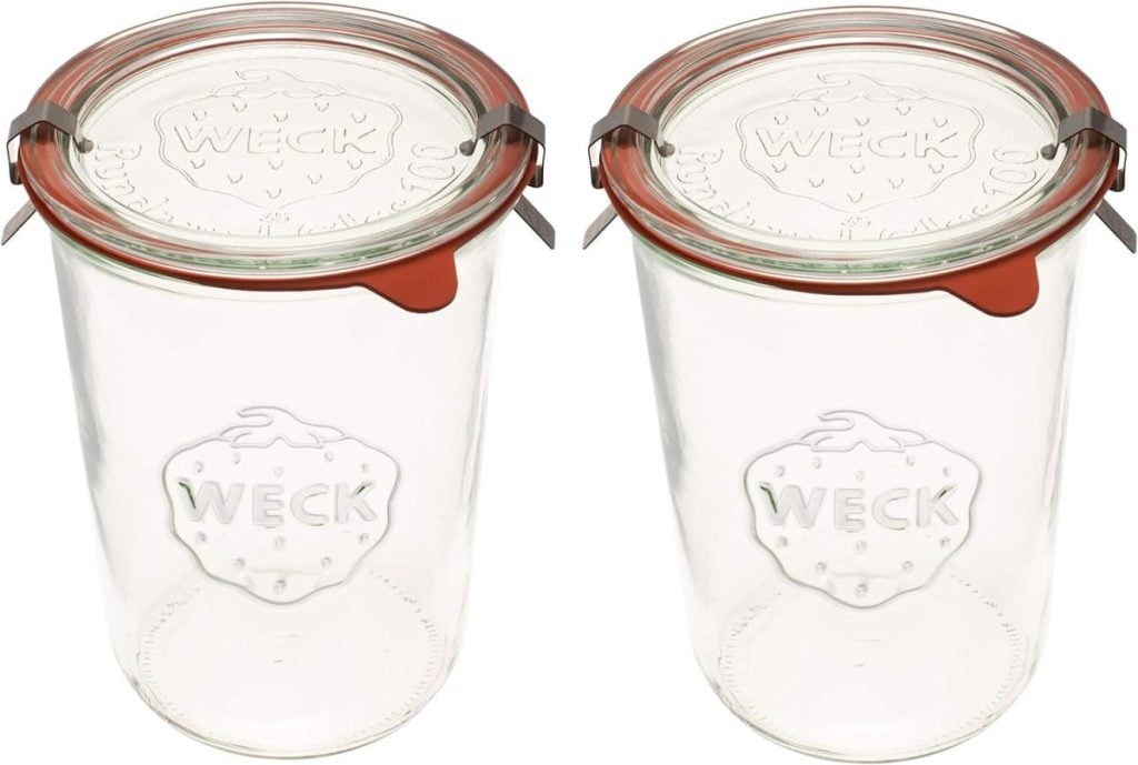 Two clear glass Weck jars with orange rubber seals and metal clips, each embossed with a strawberry logo on the front.