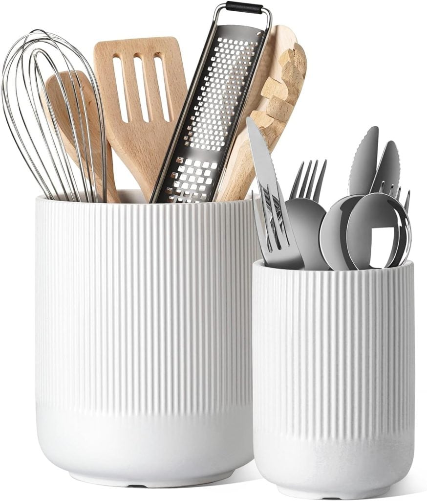 Two white ribbed ceramic holders, perfect for any Amazon Prime kitchen haul, contain various utensils including wooden spatulas, a whisk, a grater, and silverware.