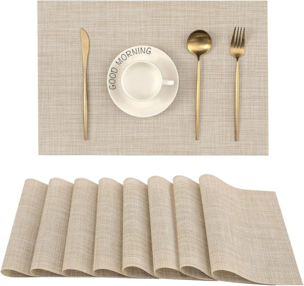 A beige woven placemat set with gold knife, spoon, fork, a white "GOOD MORNING" cup and saucer, and elegant glass water bottles arranged on top.
