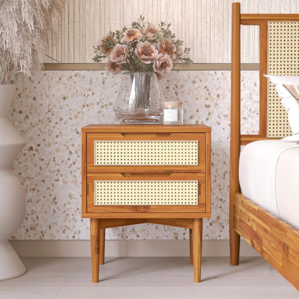 A wooden nightstand with two rattan-accented drawers sits beside a bed, holding a bouquet of pink flowers in a clear vase and a candle. Nearby, a large white vase adds elegance to the scene. Available on Amazon Prime for seamless shopping convenience.