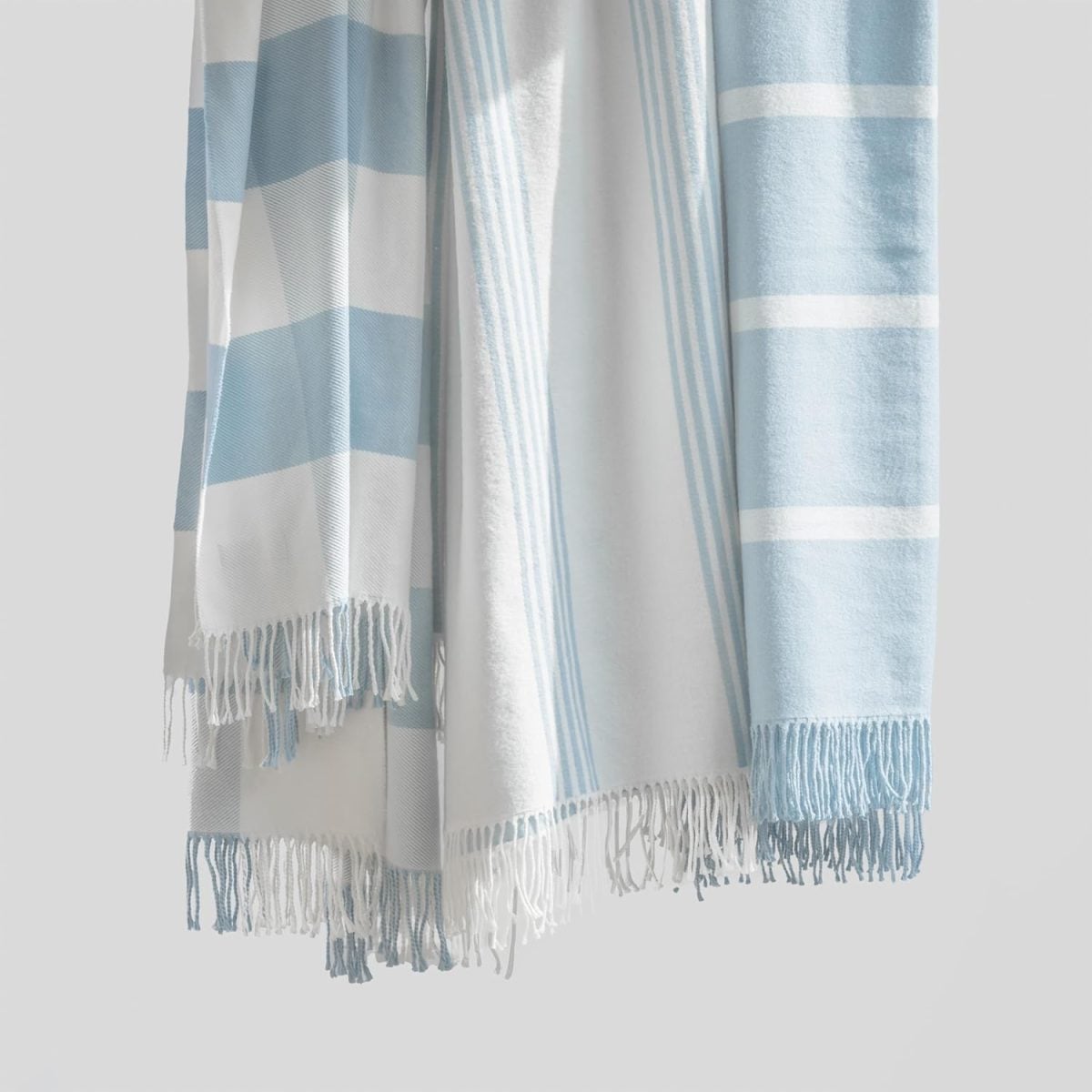 Three Serena and Lily light blue and white striped towels with fringed edges hang against a plain light background.