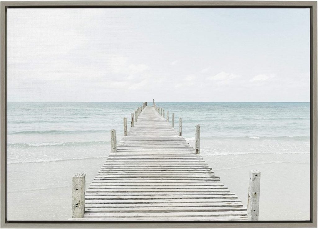 A wooden pier extends into the calm ocean under a clear sky, with waves gently lapping at the shore.