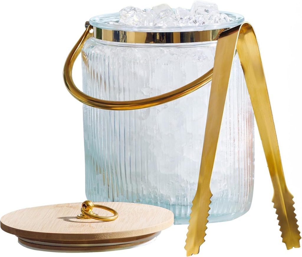 A clear ribbed glass ice bucket filled with ice cubes, featuring a gold metal handle and matching tongs, sits beside elegant glass water bottles; a wooden lid with a gold ring rests nearby.