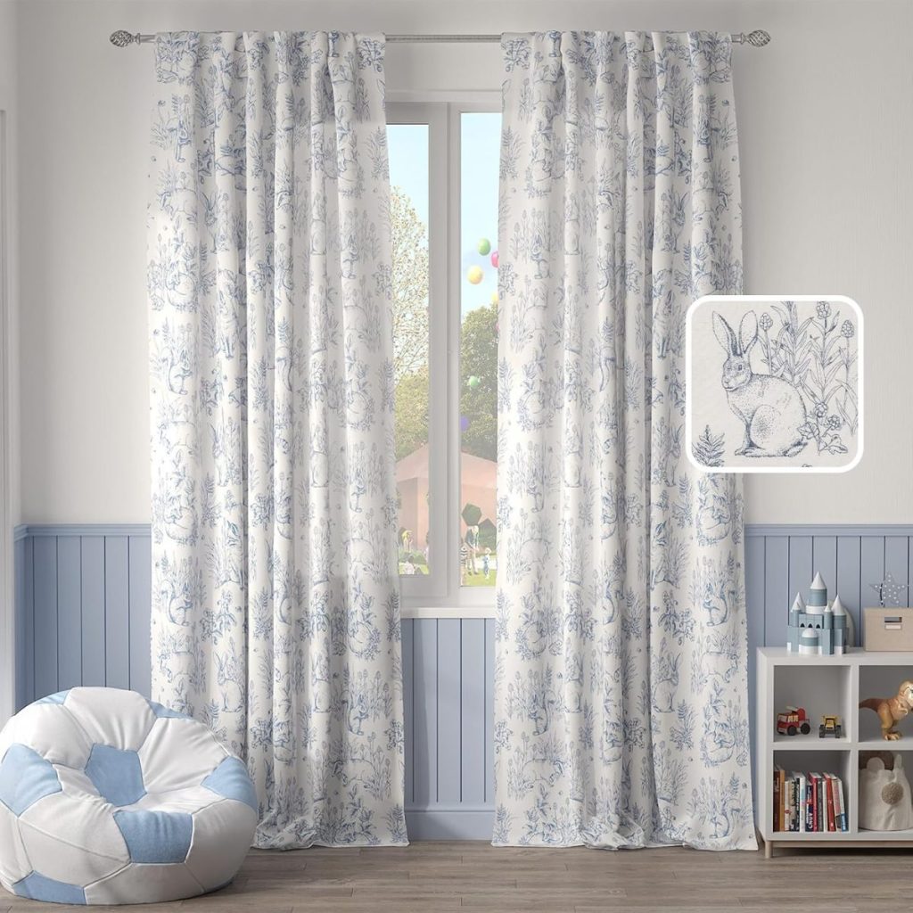 A bright room with blue and white curtains featuring rabbit designs, a bean bag chair, and a small shelf with toys and books next to a window overlooking a garden.