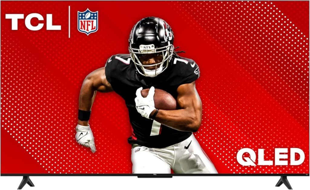 A football player in a black uniform holds a ball, vividly displayed on a red TCL QLED TV screen featuring NFL branding, ready for action. Catch the game live with Amazon Prime.