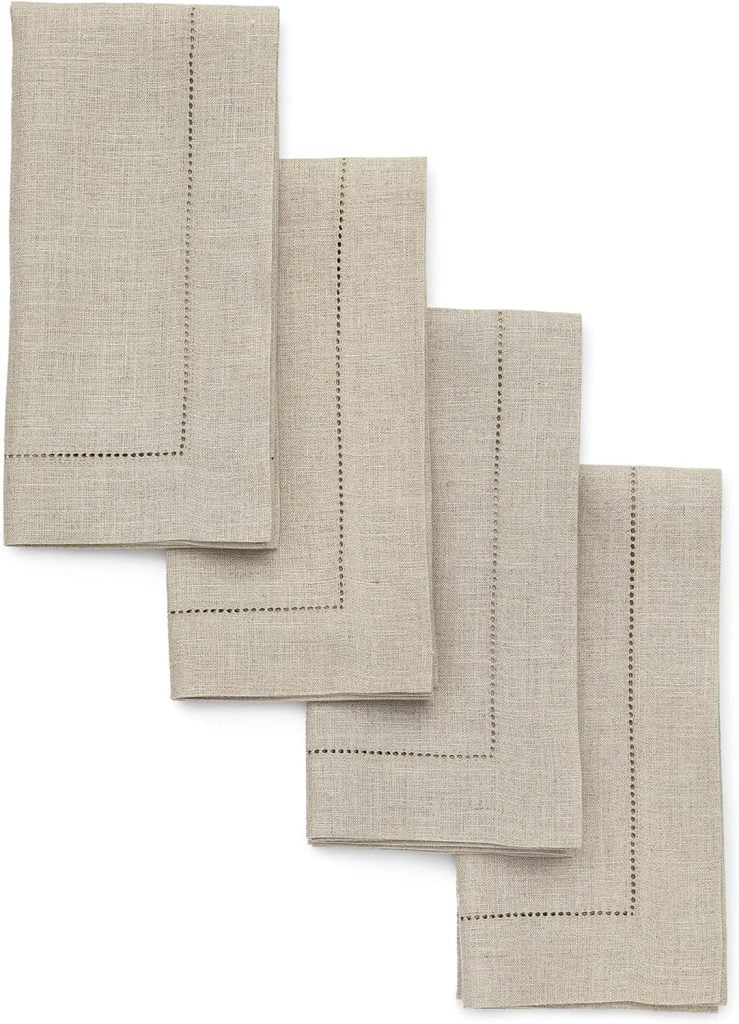 Four beige linen napkins with decorative stitching arranged in a staggered stack, perfect for adding an elegant touch to your Thanksgiving plates.