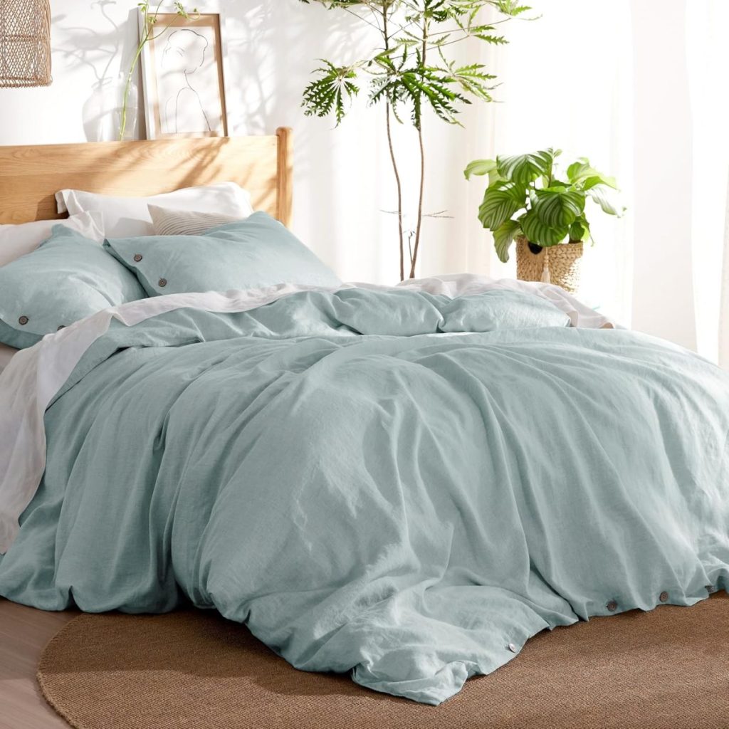 A neatly made bed with light green bedding, two pillows, and a wooden headboard. The room has a round rug, a small tree in a pot, and a potted plant on a table.