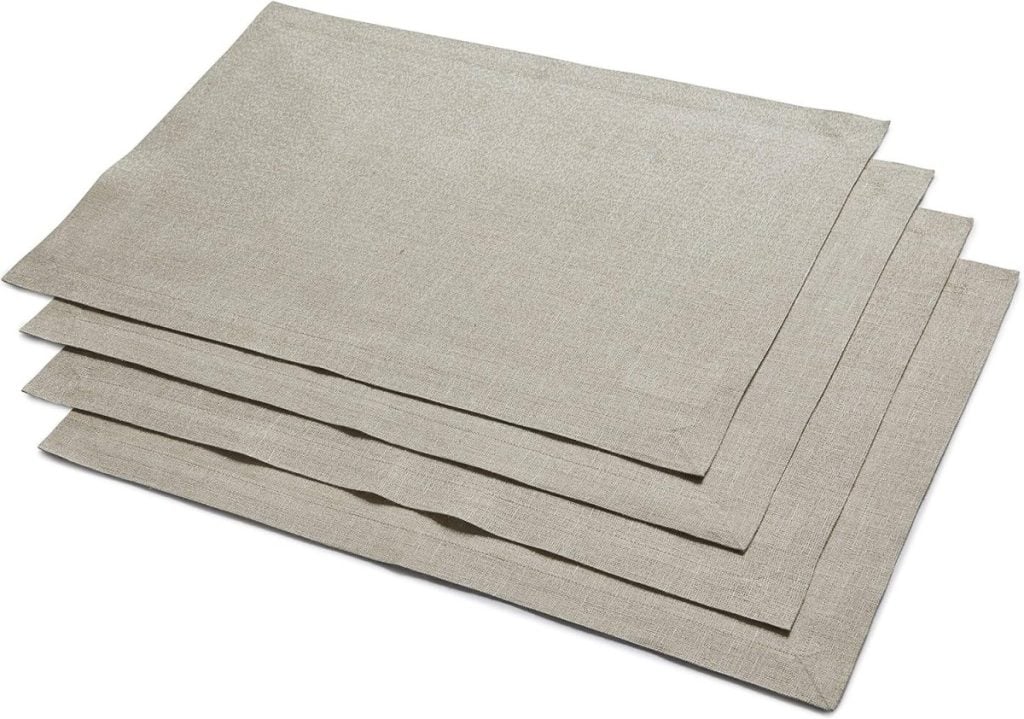 Four beige cloth placemats, perfect for your Thanksgiving plates, stacked neatly on top of each other against a crisp white background.