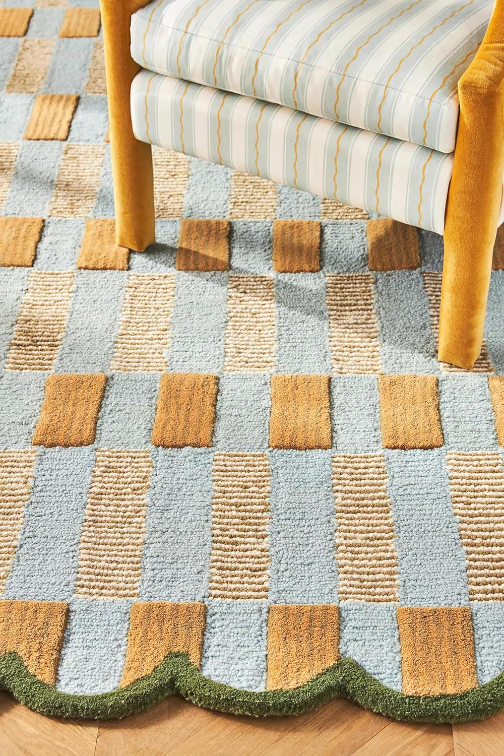 A Serena and Lily patterned rug with a blue and tan checkerboard design and a scalloped green edge, under a yellow chair with striped upholstery.