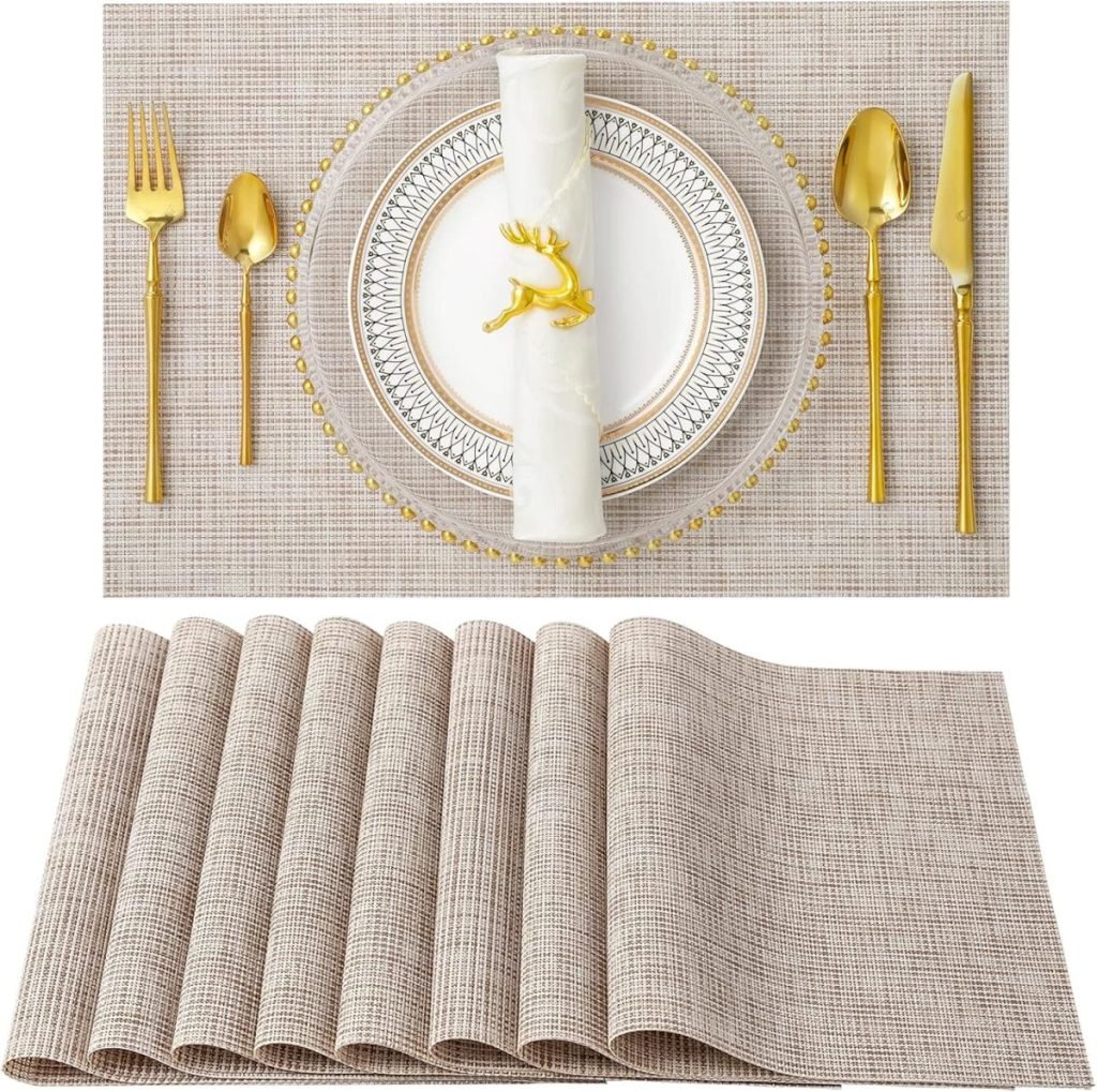 A dining setup with a gold fork, knife, and spoon beside a decorative plate featuring a deer. A rolled napkin is placed on the plate. Below, a set of seven beige placemats is displayed.