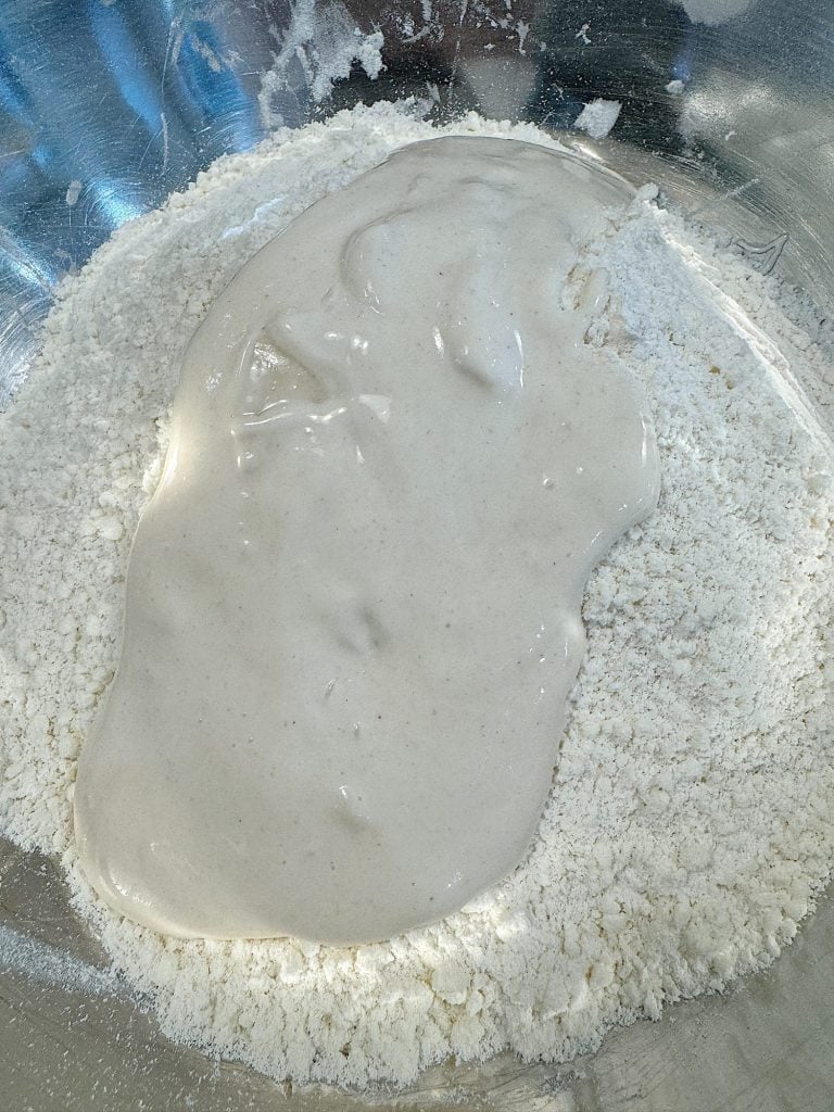 Batter being mixed with flour in a stainless steel bowl.