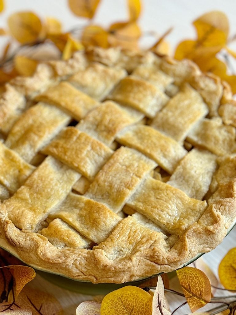 A freshly baked pie with a lattice crust, surrounded by autumn leaves.