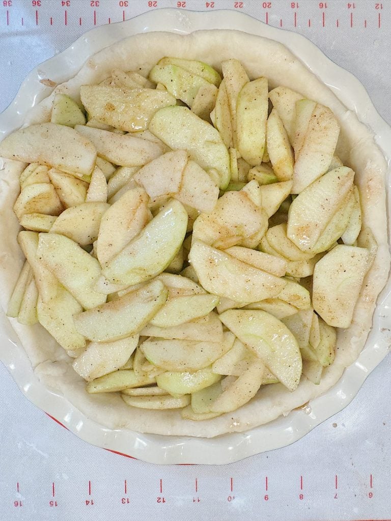 Unbaked apple pie with seasoned apple slices arranged in a crust, ready for baking.