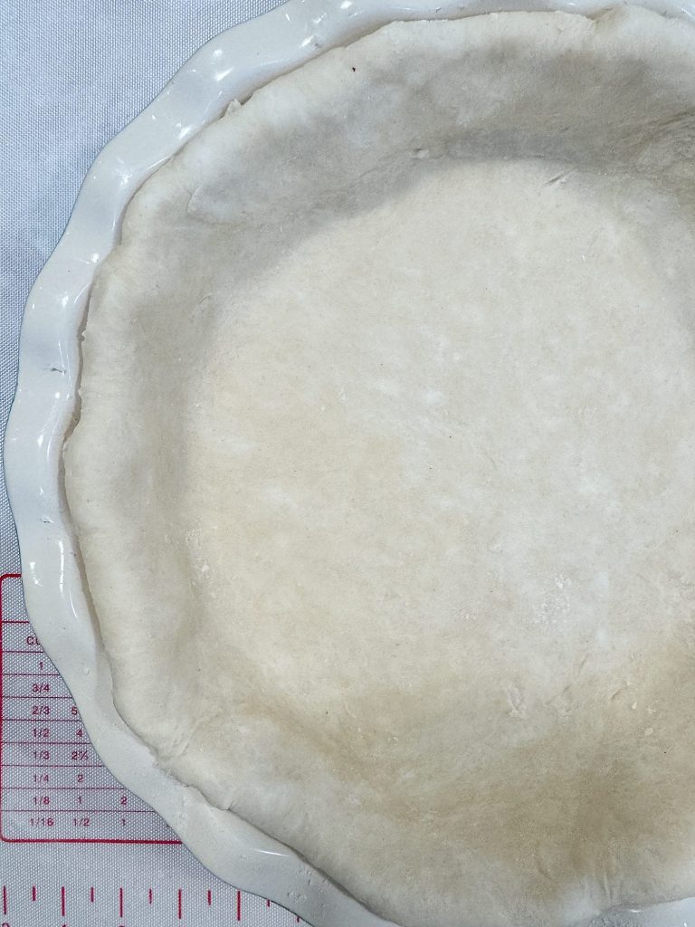 Unbaked pie crust in a white fluted dish on a measuring mat.