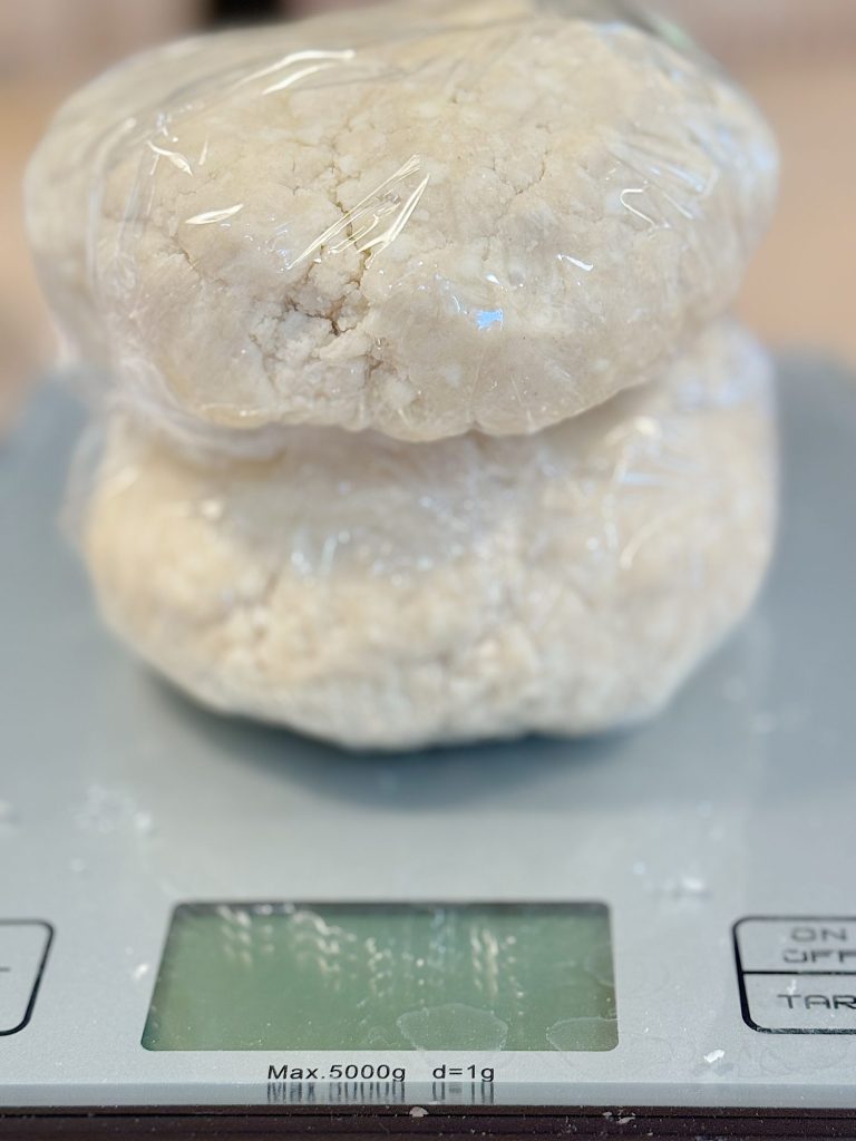 Two wrapped dough balls placed on a digital kitchen scale showing a display with numbers.