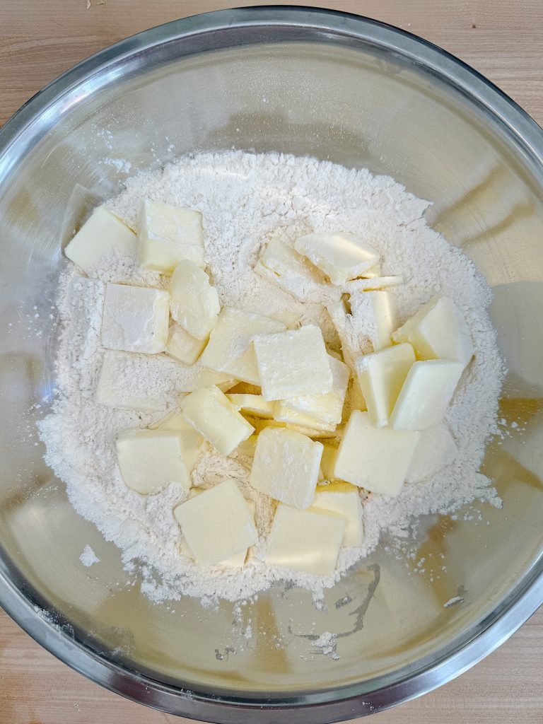 Cubed butter sits on top of flour in a stainless steel mixing bowl, ready for pastry preparation.