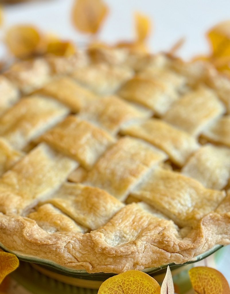 A freshly baked pie with a golden, lattice-style crust surrounded by autumn leaves.