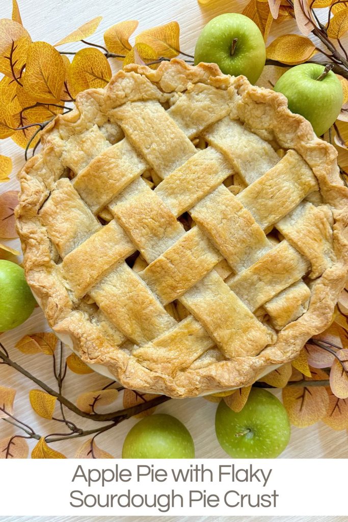 A lattice-topped apple pie on a decorative surface with green apples and yellow leaves around it.