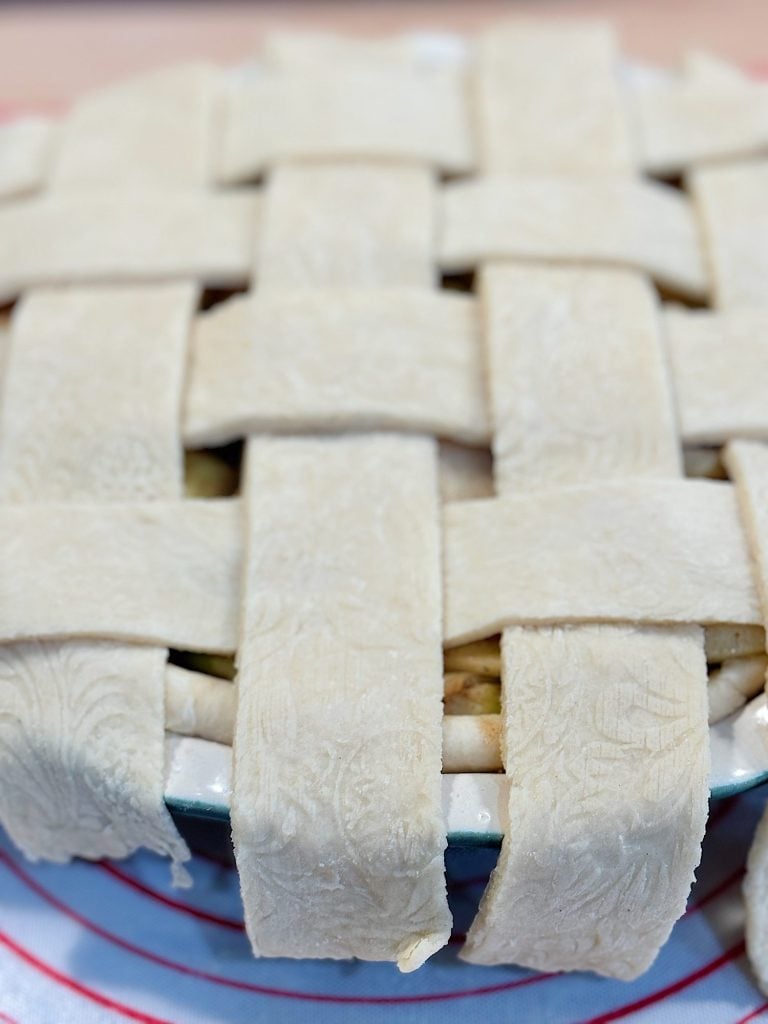 A pie with a lattice crust pattern, unbaked, placed in a pie dish on a circular silicone mat.