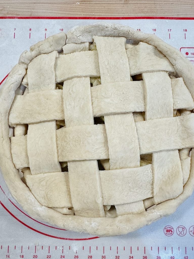 Unbaked pie with a lattice crust on a red and white baking mat.