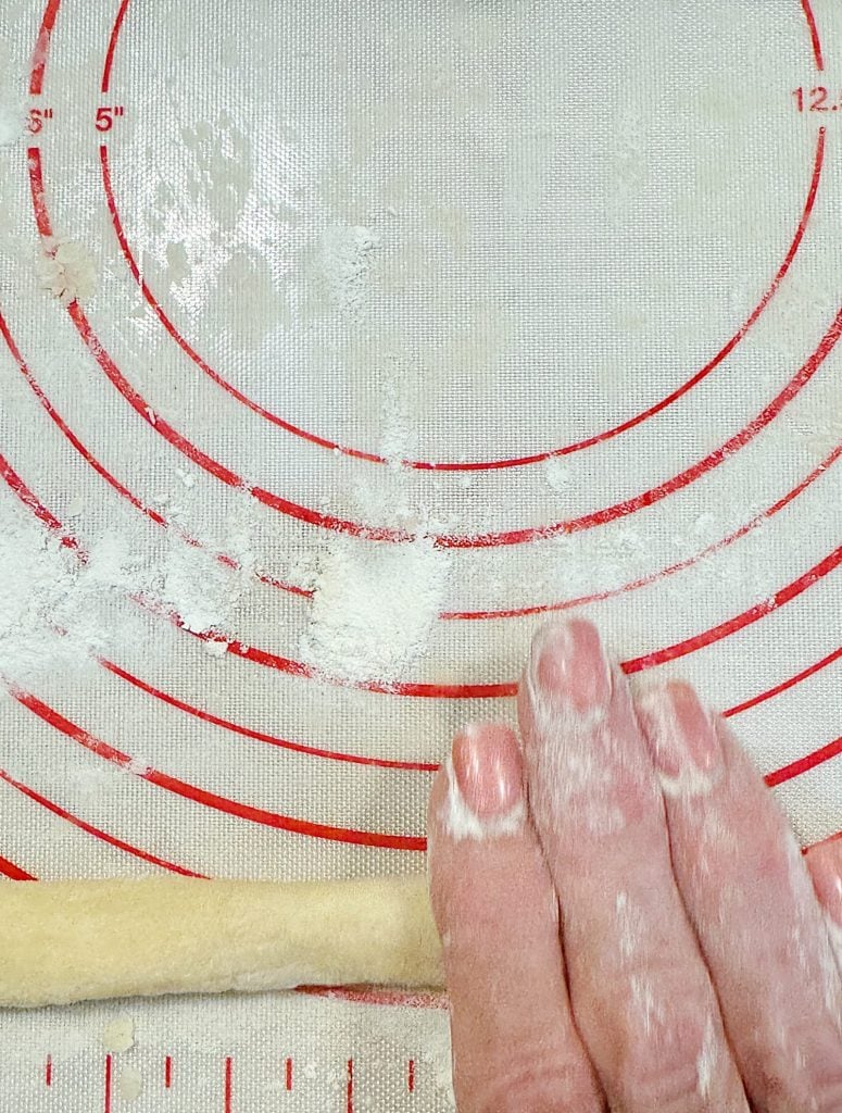 Hands rolling dough on a floured silicone mat with measurement markings.