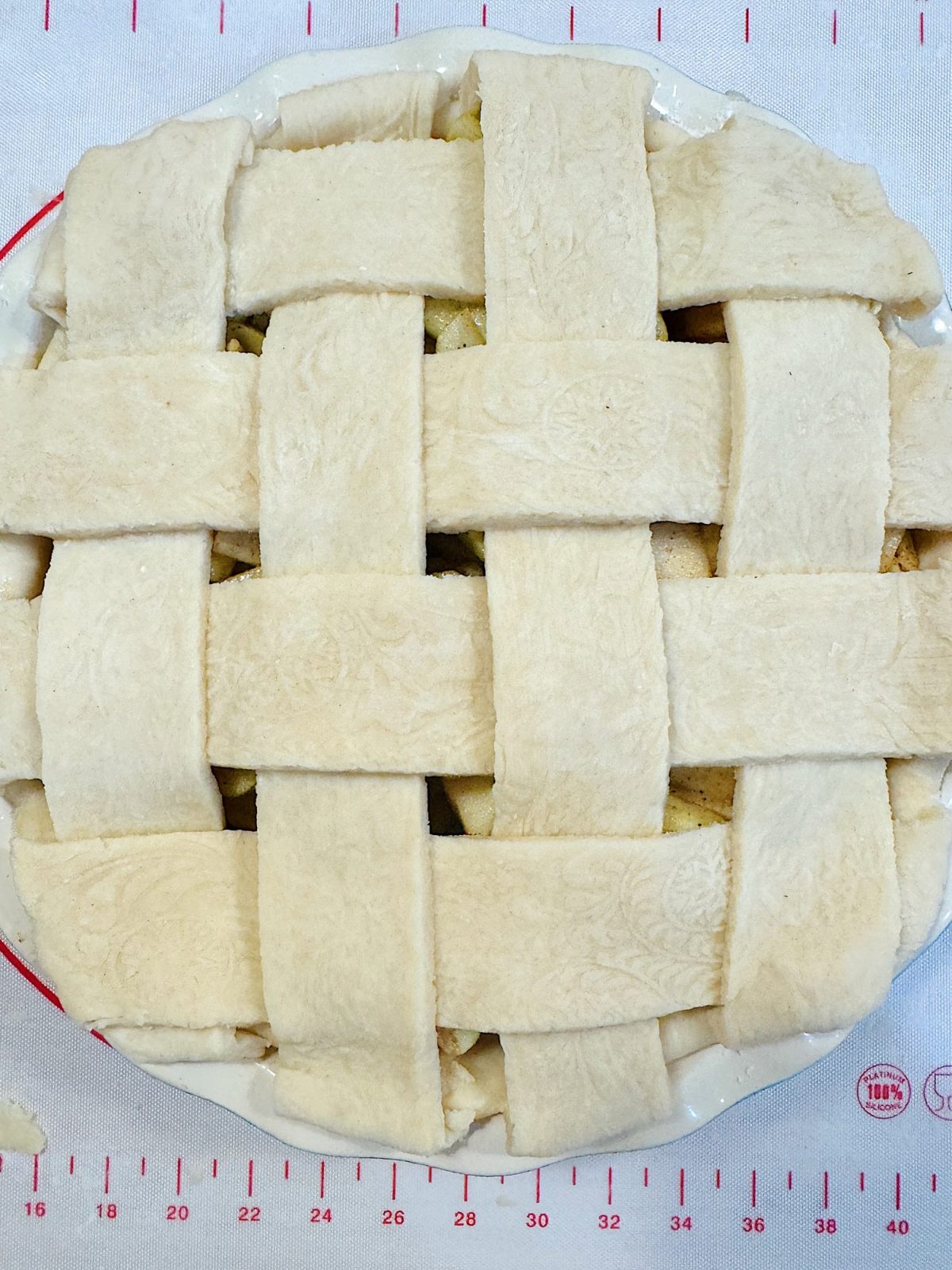 Unbaked pie with a lattice crust in a white dish, placed on a measuring mat.