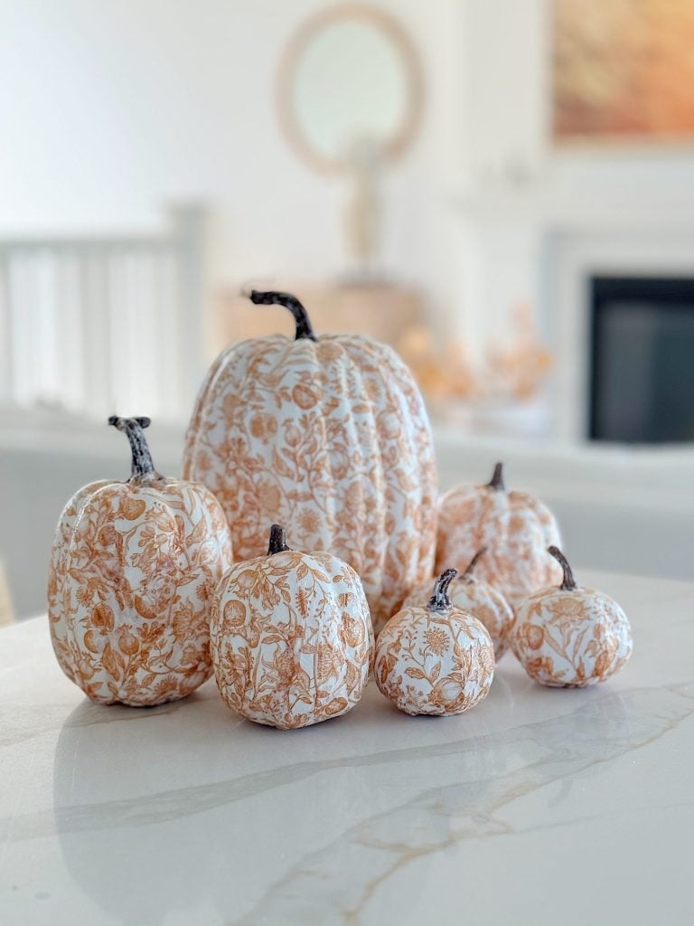 Six decorative pumpkins with a floral pattern are arranged on a light-colored marble surface.