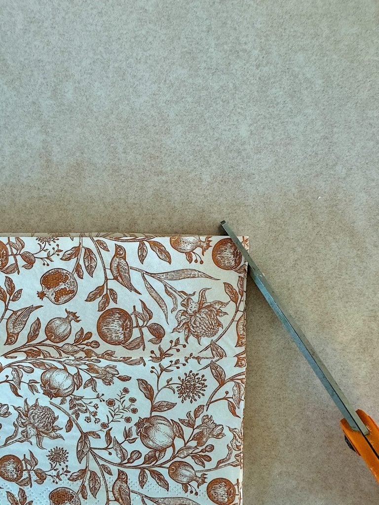 Scissors cutting a piece of floral patterned brown fabric on a beige surface.