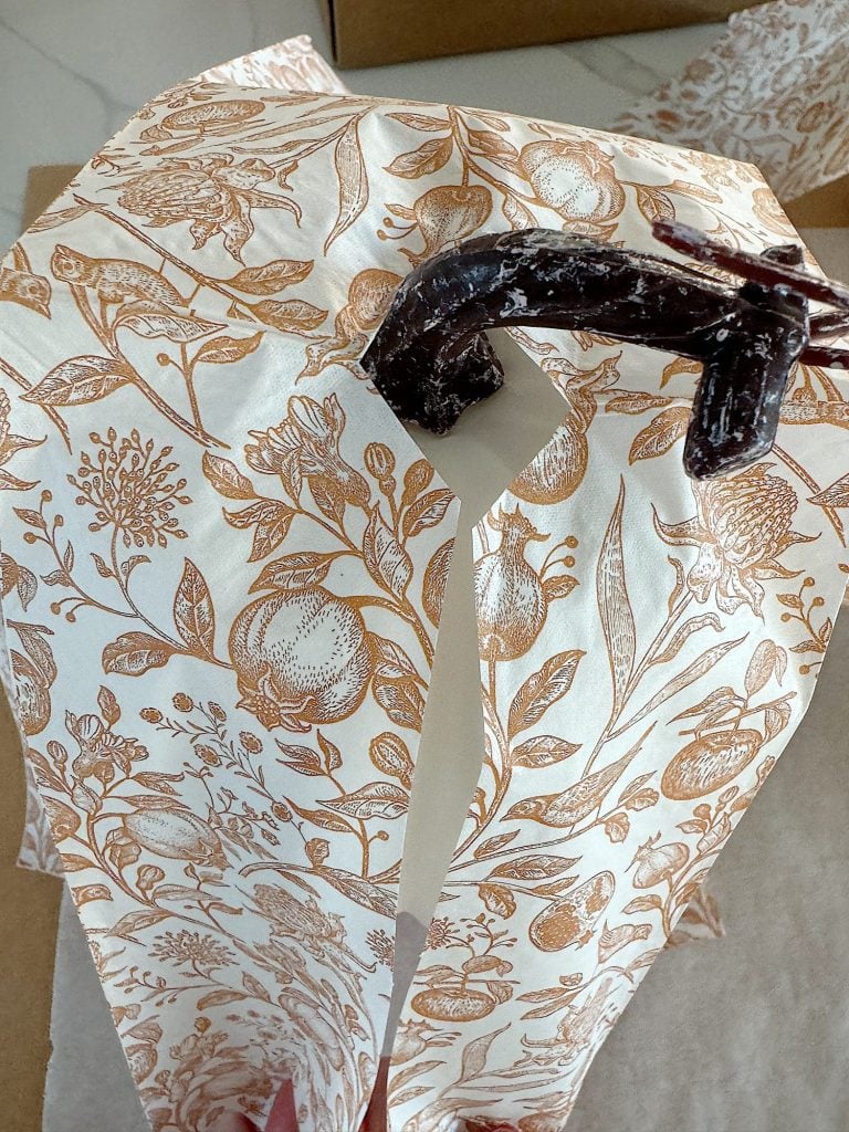 Decorative paper with a brown floral pattern is partially cut by scissors.