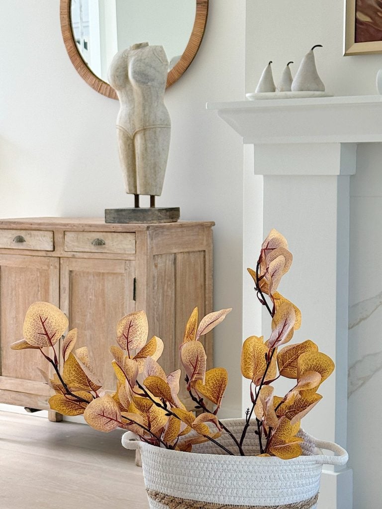 A living room with a wooden cabinet, abstract sculpture, round mirror, and a potted plant with yellow leaves.