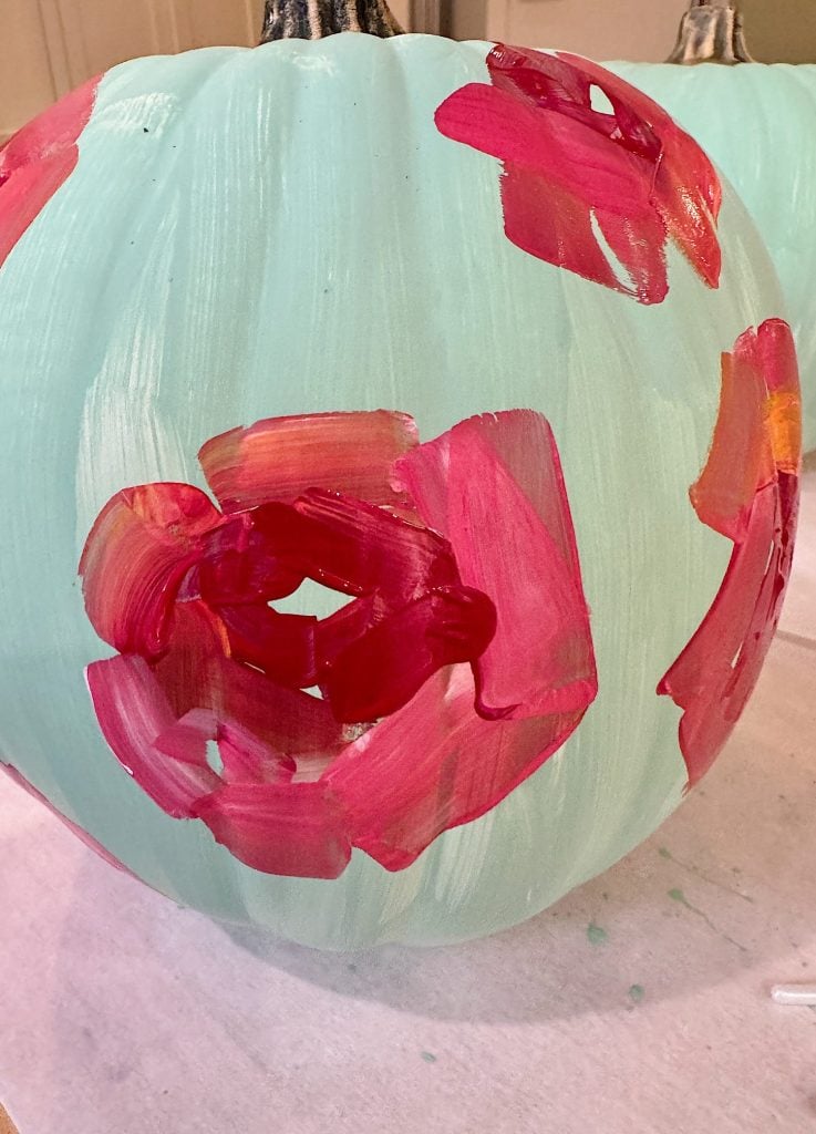 A pumpkin painted light blue with abstract red and pink flower designs.