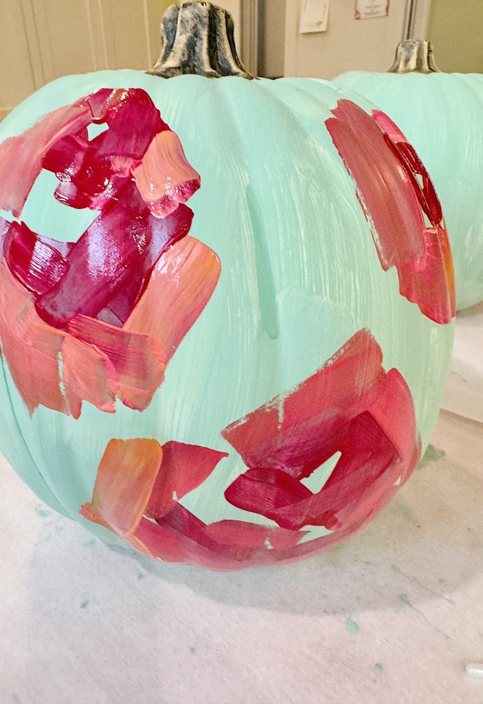 A light blue pumpkin with abstract red and pink brush strokes painted on its surface.