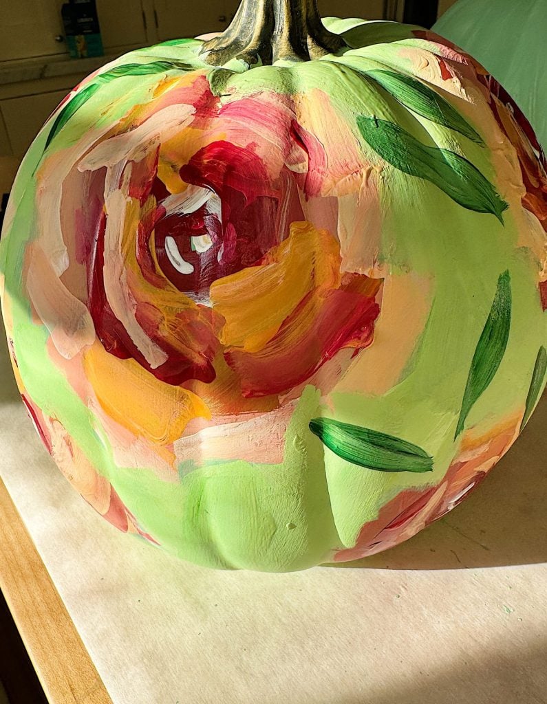 A round object painted with colorful floral patterns, featuring reds, pinks, and greens, is placed on a light-colored surface.