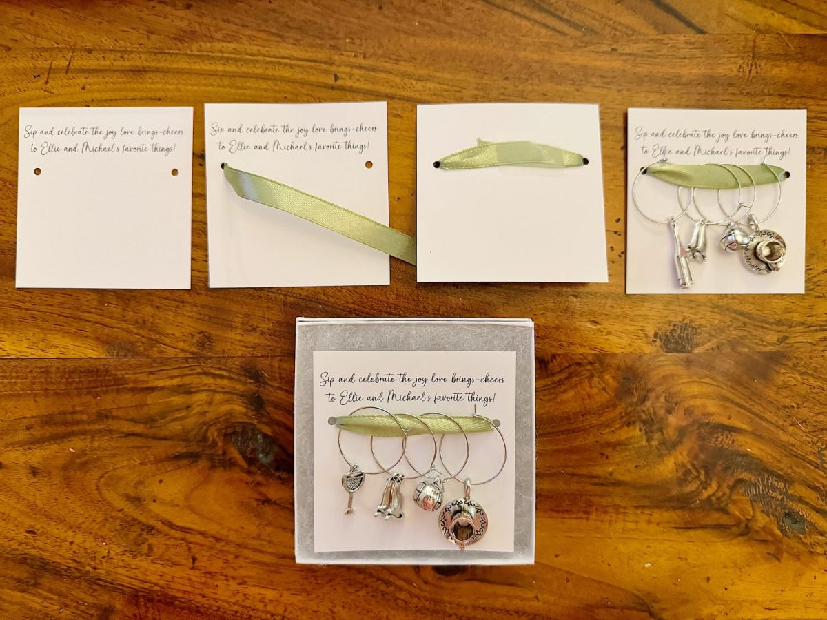A set of charm keychains displayed on a wooden surface. Cards with green ribbons are placed above, showing two holes each. The central card has keychains attached, featuring various charms.