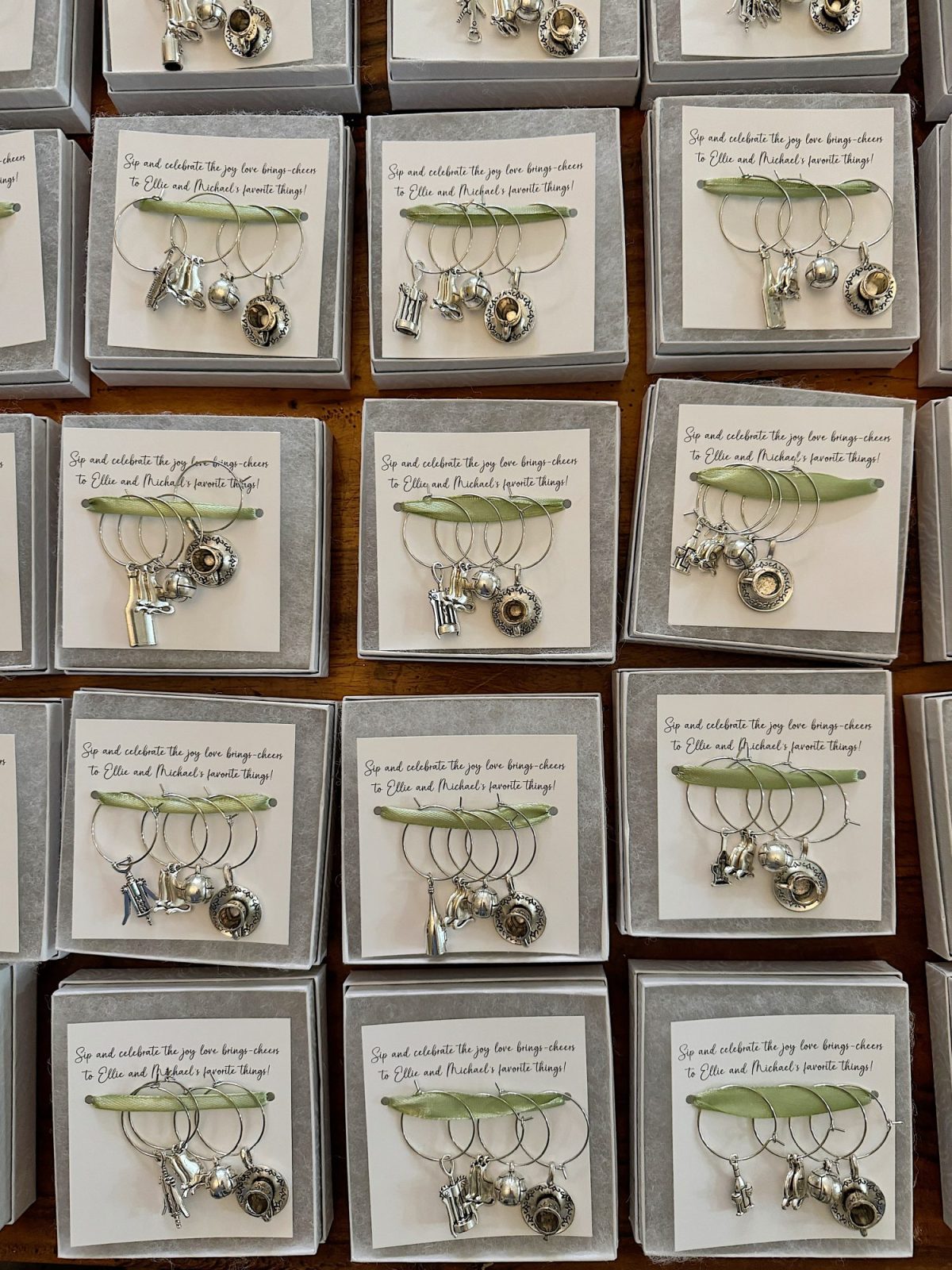 Multiple sets of wine glass charms with various charms are displayed in boxes with celebratory messages.