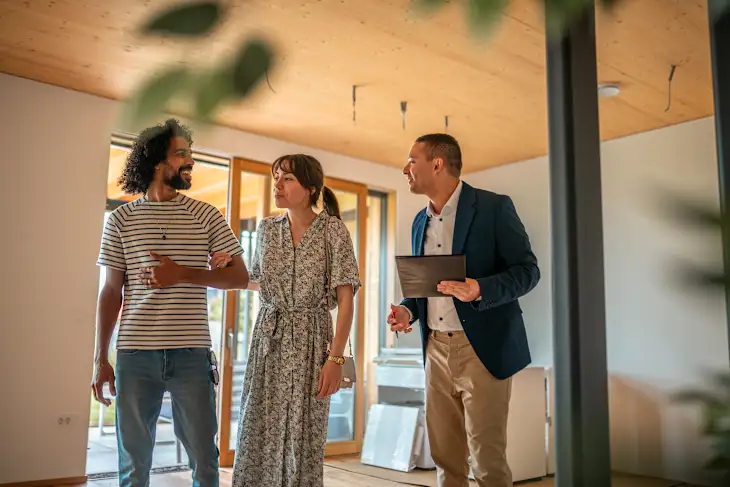 A couple tours a house with a real estate agent holding a tablet.