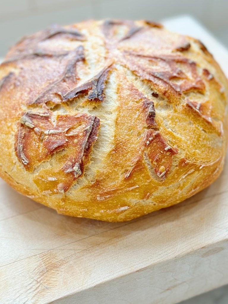 Loaf of artisan bread with a crusty golden-brown top on a light-colored cutting board.