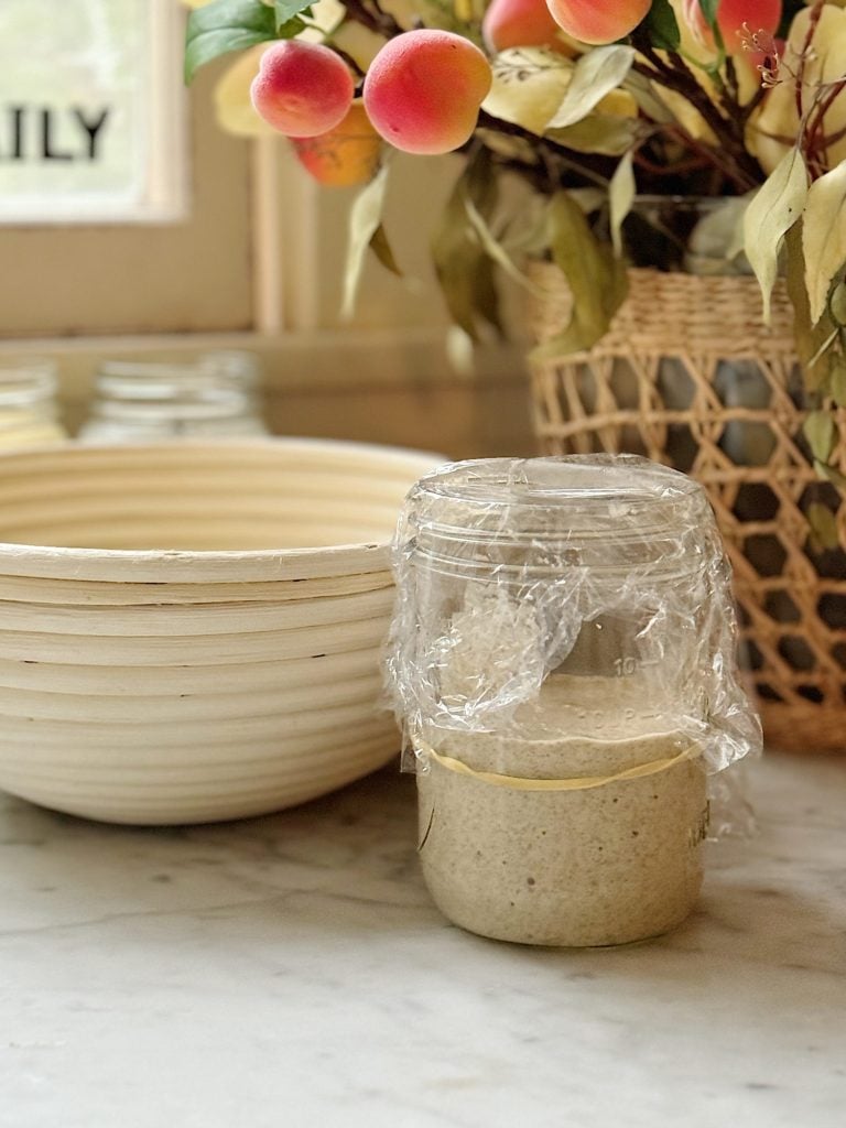 Glass container with sourdough starter wrapped in plastic wrap.